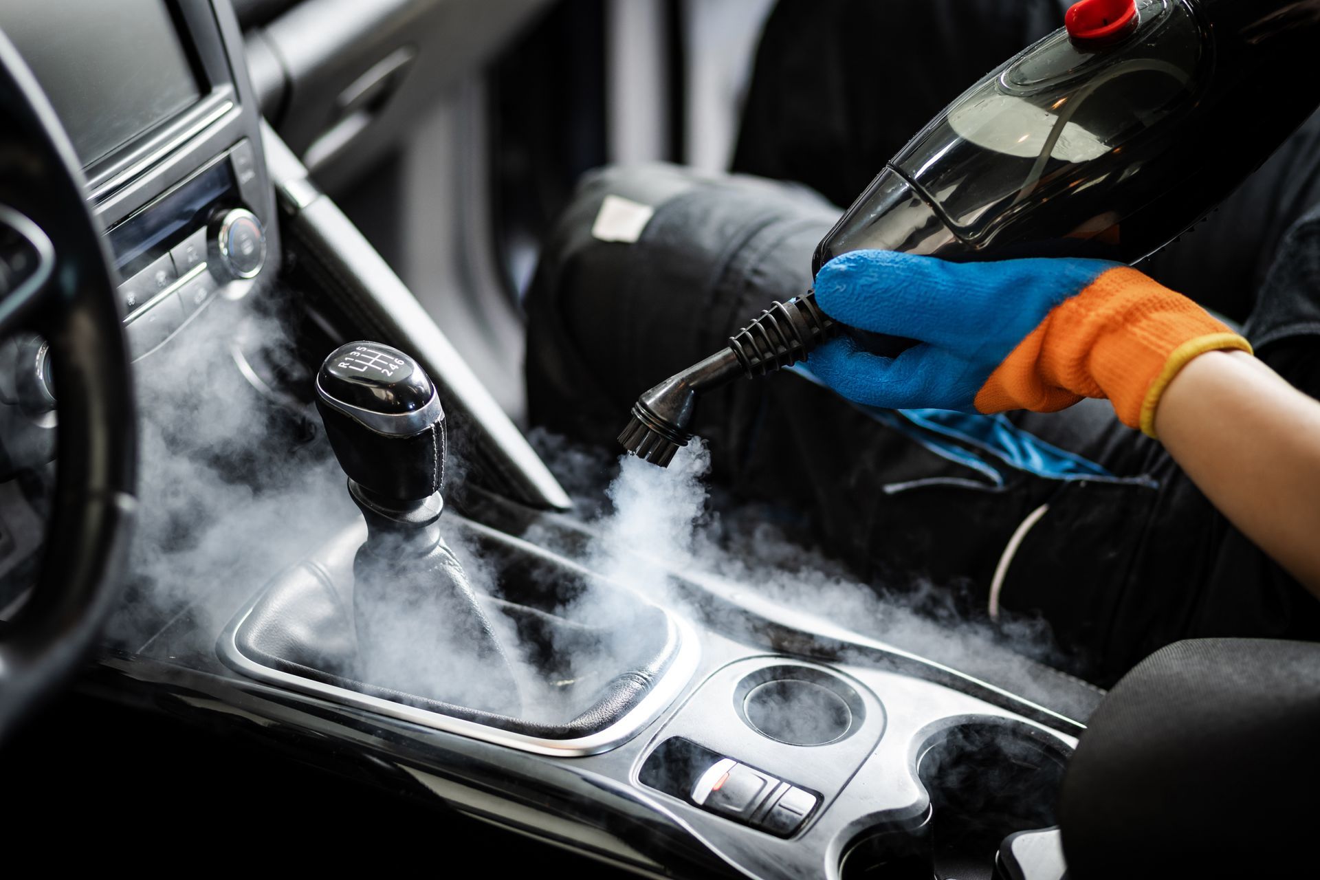 Une personne nettoie et désinfecte la console centrale et le levier de vitesse d'une voiture avec un appareil à vapeur.