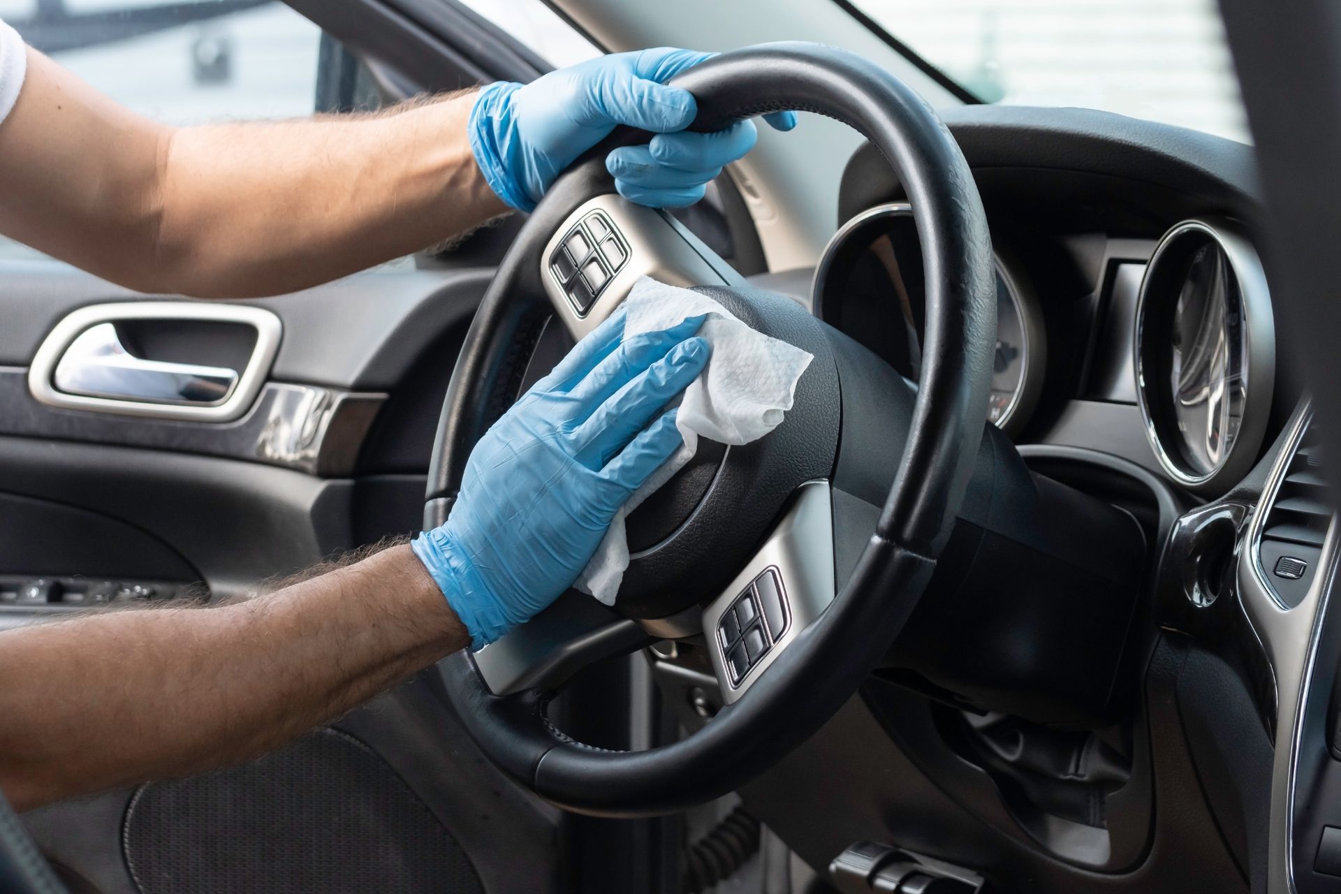 Des mains gantées nettoient le volant d'une voiture avec un chiffon.