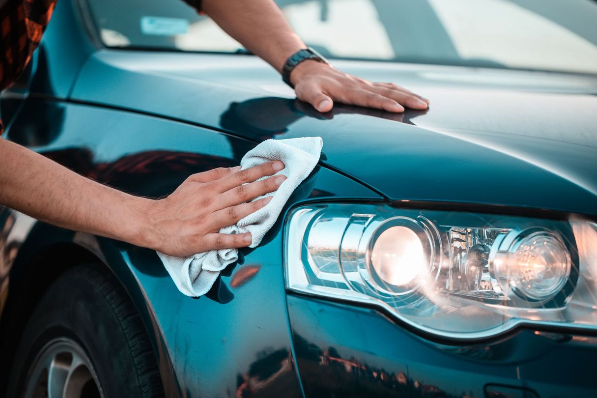 Des mains essuient le phare et le capot d'une voiture avec un chiffon.