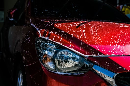 Carrosserie d'une voiture rouge recouverte de savon dans une station de lavage.