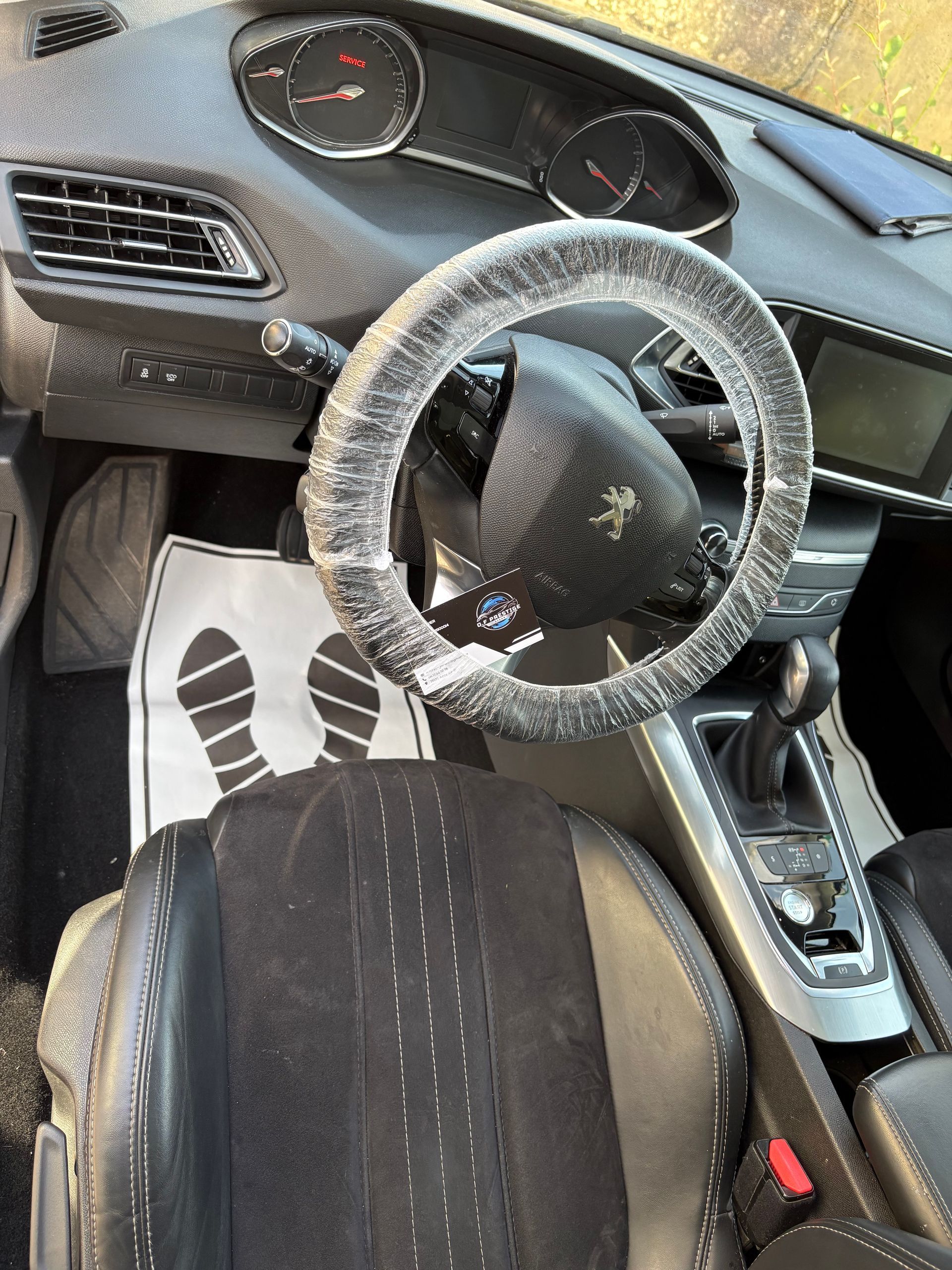 Intérieur d'une Peugeot avec couvre volant et sièges noirs, vu du siège conducteur.