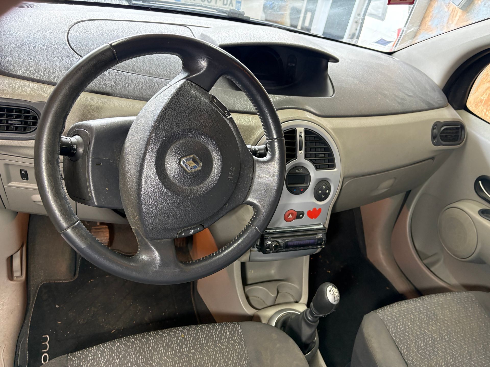 Intérieur de voiture avec volant, levier de vitesse manuel et console centrale sur un tableau de bord beige.