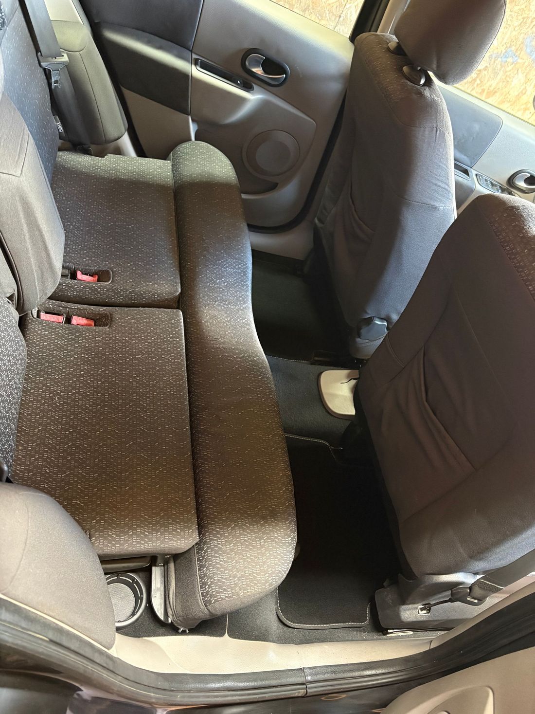 Intérieur de la voiture avec sièges arrière rabattus créant un espace de chargement plat, sellerie en tissu foncé visible.