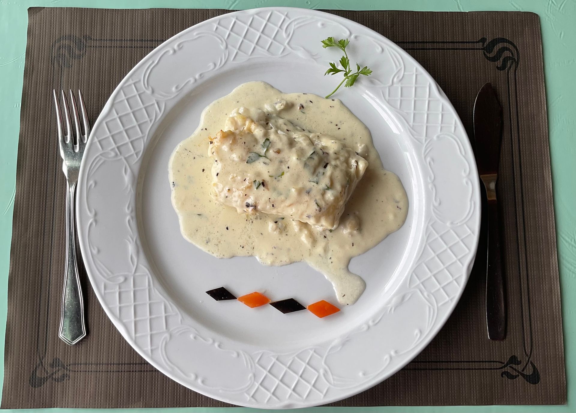 Plato principal de pollo cremoso con champiñones servido con cuchillo y tenedor en una mesa de madera.