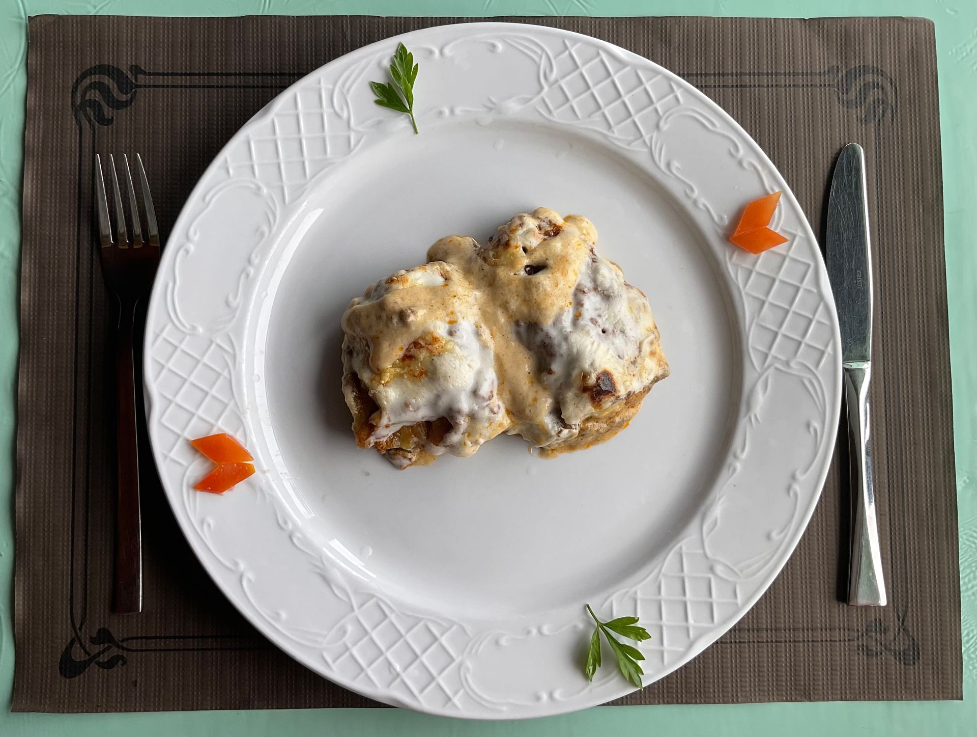 Dos bocaditos horneados con queso en un plato blanco con guarnición, colocados sobre un mantel individual gris con cubiertos.