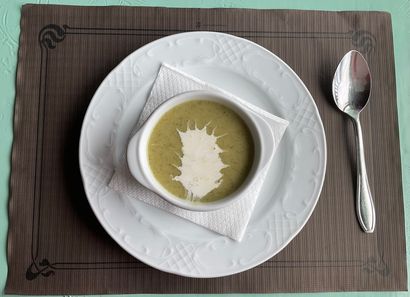 Sopa servida en un tazón blanco sobre un plato con una cuchara, todo colocado sobre un mantel individual marrón.