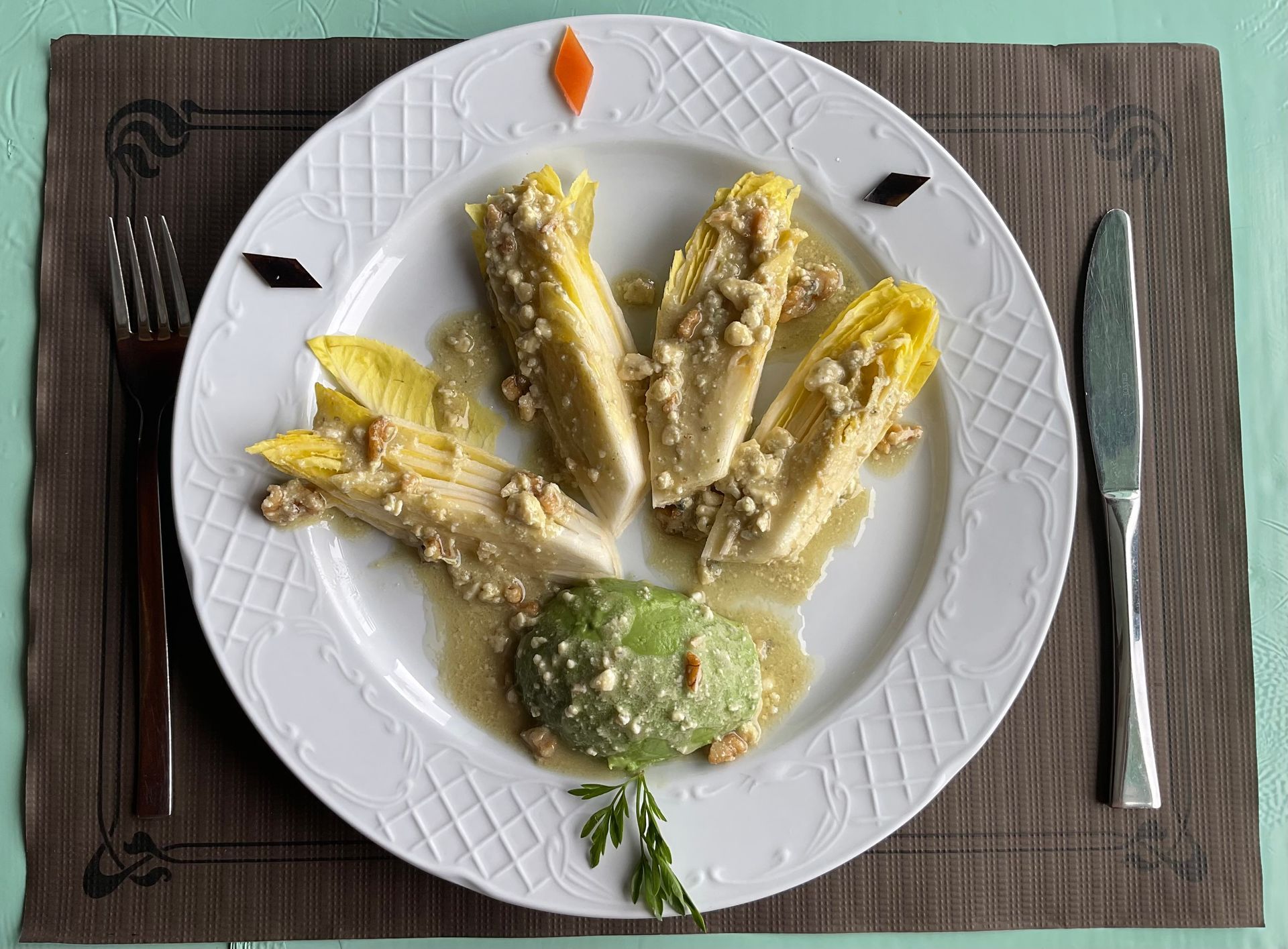 Plato de endivias rellenas con salsa cremosa y guarnición verde, servido sobre un mantel individual con cubiertos.