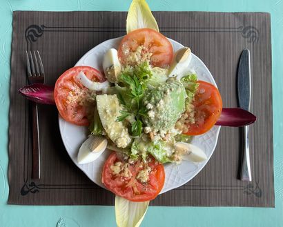 Ensalada colorida de tomates, verduras y rodajas de limón en un plato blanco sobre un mantel individual oscuro.