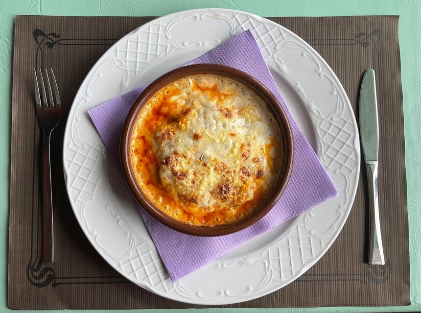 Cazuela al horno en una fuente pequeña sobre un plato blanco con una servilleta morada, tenedor y cuchillo sobre una bandeja gris.