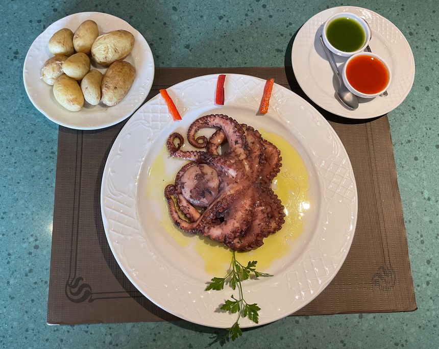Pulpo a la parrilla en un plato blanco con salsas, panecillos y hierbas en un plato de mesa.