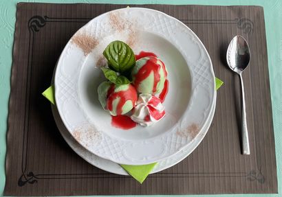 Plato de postre con fresas, crema batida y menta en un plato blanco, con una cuchara al lado.