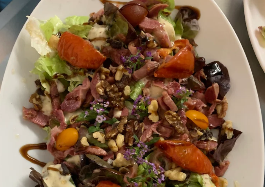 Des lardons, tomates, noix, gésiers et de la salade dans une assiette claire