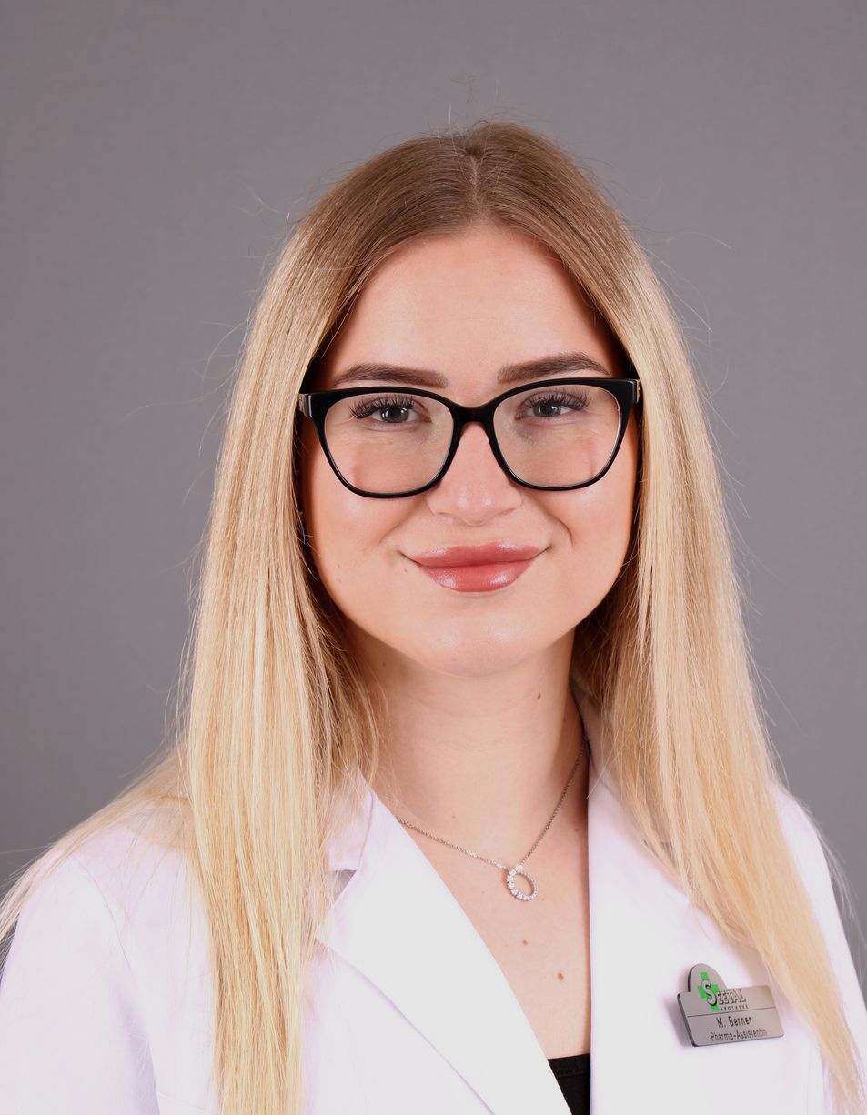 Frau mit blonden Haaren, Brille und weißem Laborkittel lächelt in die Kamera.