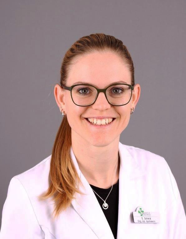 Frau mit Brille und Pferdeschwanz lächelt im weißen Kittel.