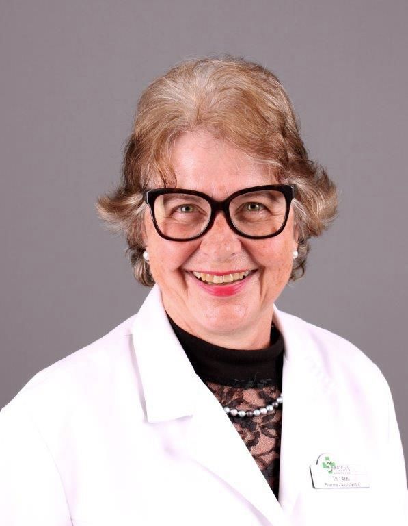 Frau im weißen Laborkittel, Brille, lächelnd. Grauer Hintergrund.