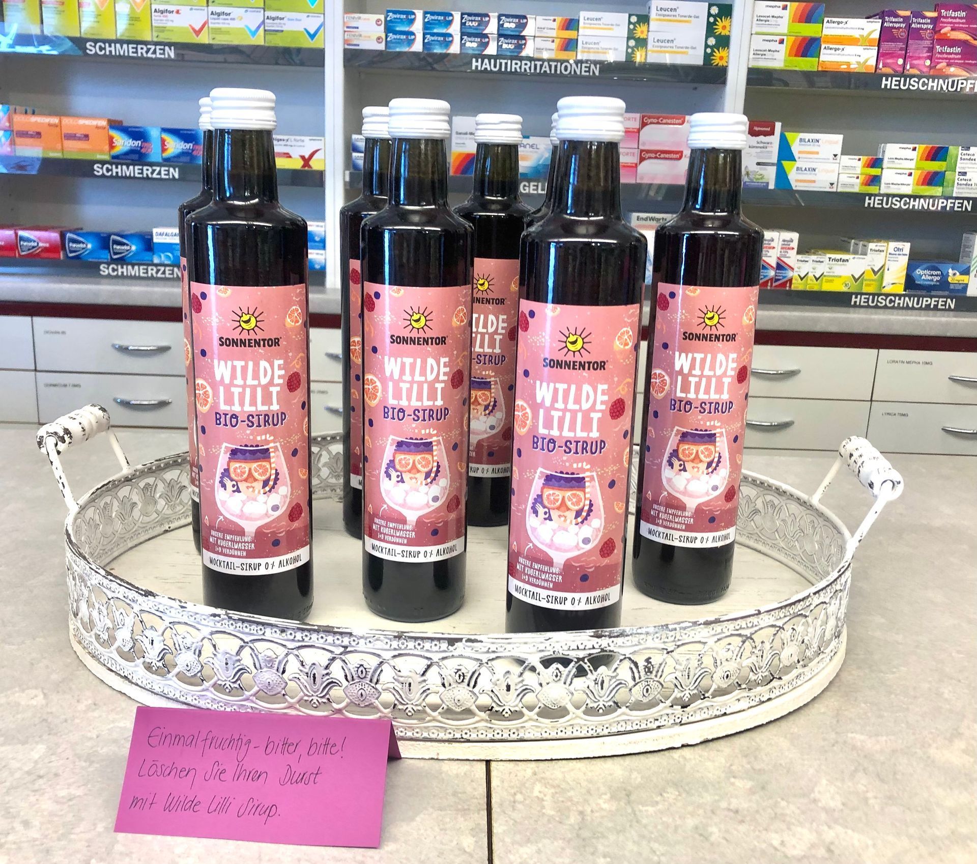 Flaschen „Wilde Lilli“-Likör auf einem dekorativen Tablett, ausgestellt in einem Ladenlokal, mit Preisschild.