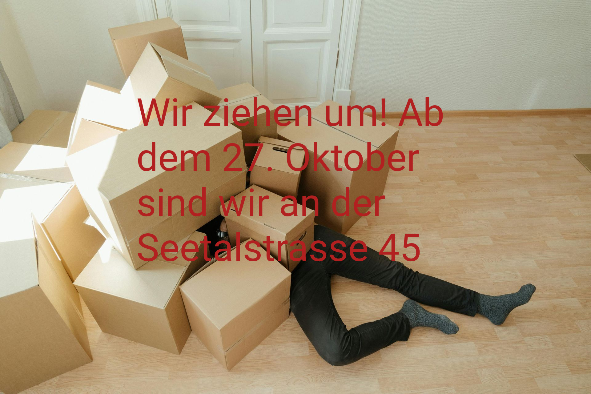 Person unter einem Stapel Umzugskartons begraben, Beine auf einem hellen Boden sichtbar.