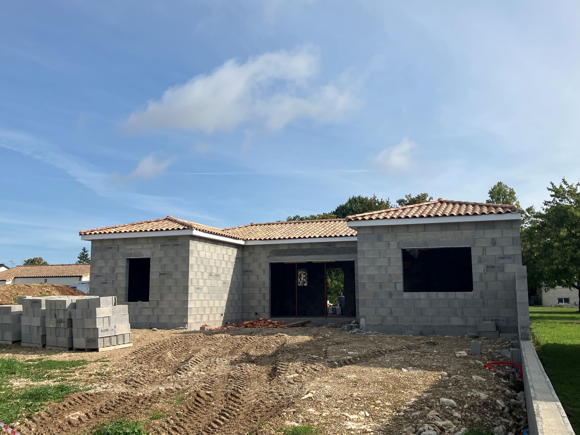 Construction d'un bâtiment d'un étage aux murs en bloc gris, sous un ciel bleu.