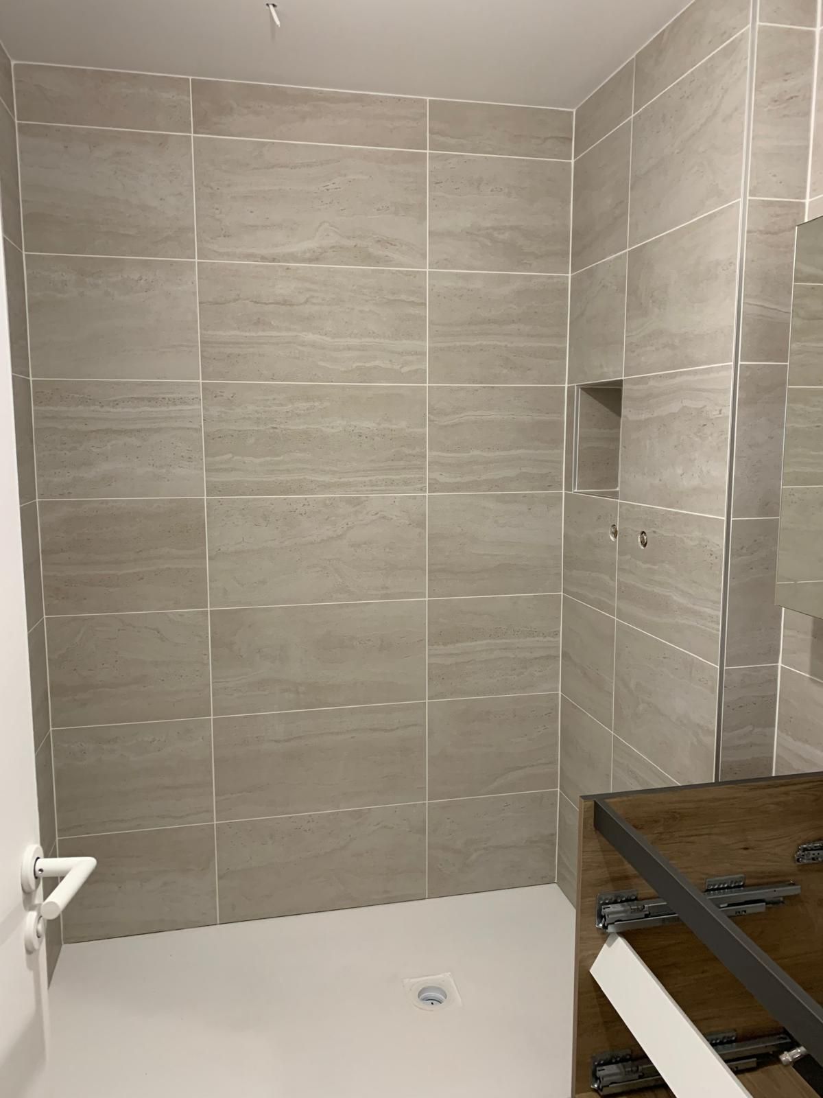 Salle de bains moderne avec douche à l'italienne carrelée, niche encastrée et meuble-lavabo en bois au premier plan.