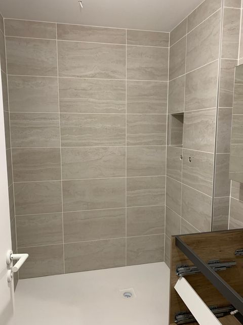 Salle de bains moderne avec douche à l'italienne carrelée, niche encastrée et meuble-lavabo en bois au premier plan.