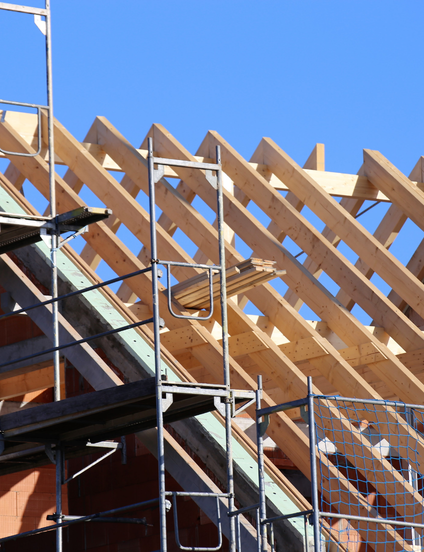 Construction d'un toit avec poutres en bois, sous un ciel bleu clair. Échafaudage visible.
