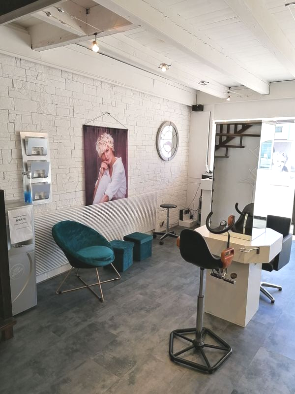Intérieur d'un salon de coiffure avec fauteuil de coiffure, salle d'attente avec fauteuil et repose-pieds turquoise, et un portrait.