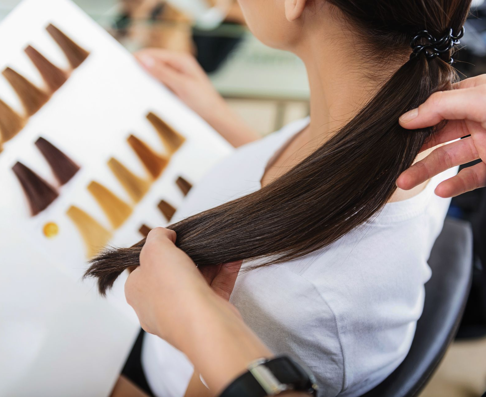 Une coiffeuse tient les cheveux foncés de sa cliente à côté d'échantillons de coloration.