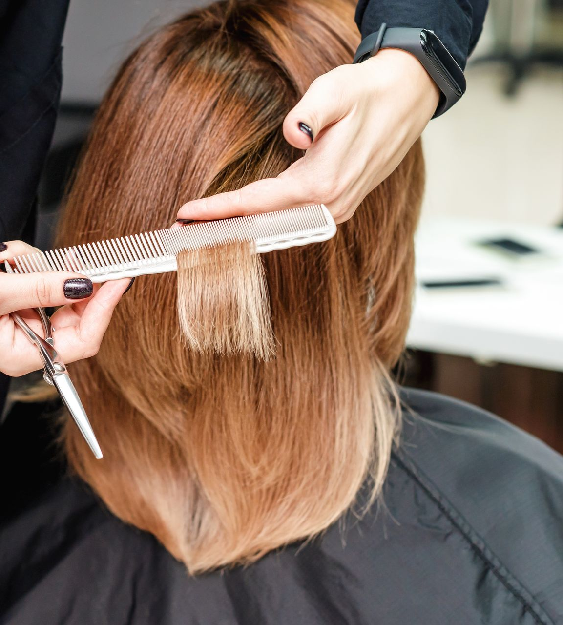 Une coiffeuse coupe les cheveux blonds d'une cliente avec un peigne et des ciseaux dans un salon de coiffure.
