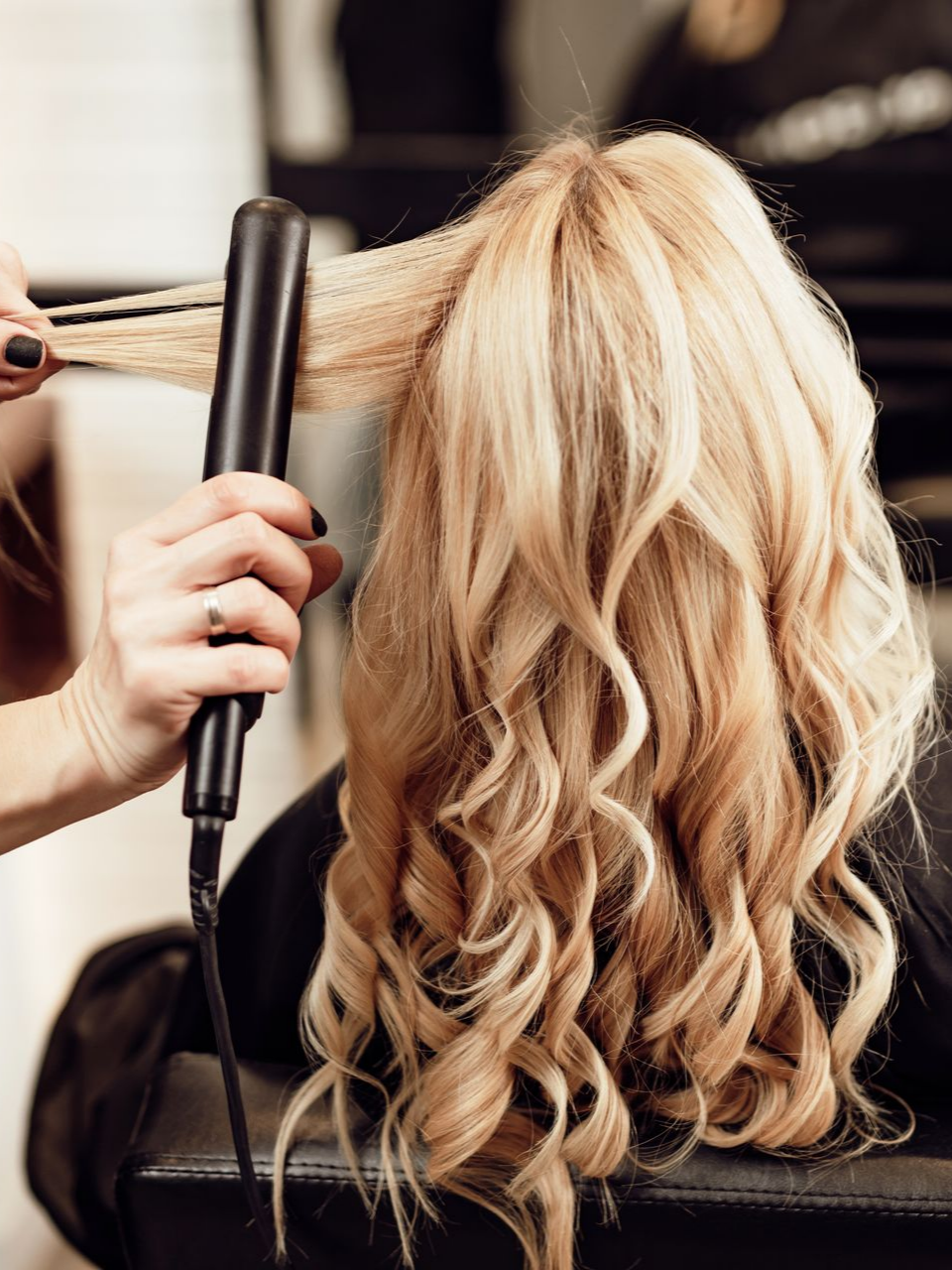 Coiffeuse utilisant un fer à lisser sur des cheveux blonds pour créer des ondulations dans un salon.