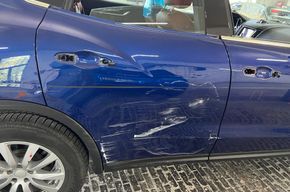 Blaues Auto mit einer großen Delle und einem Kratzer an der Seitentür und der Heckklappe.