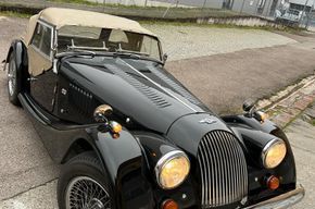 Schwarzes Oldtimer-Cabriolet, geparkt auf der Straße, schräge Frontansicht mit beigem Verdeck und runden Scheinwerfern.