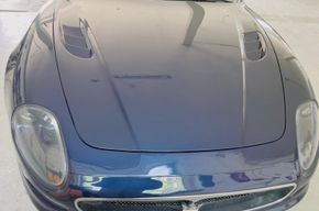 Vorderansicht eines blauen Sportwagens mit glänzender Motorhaube und runden Scheinwerfern