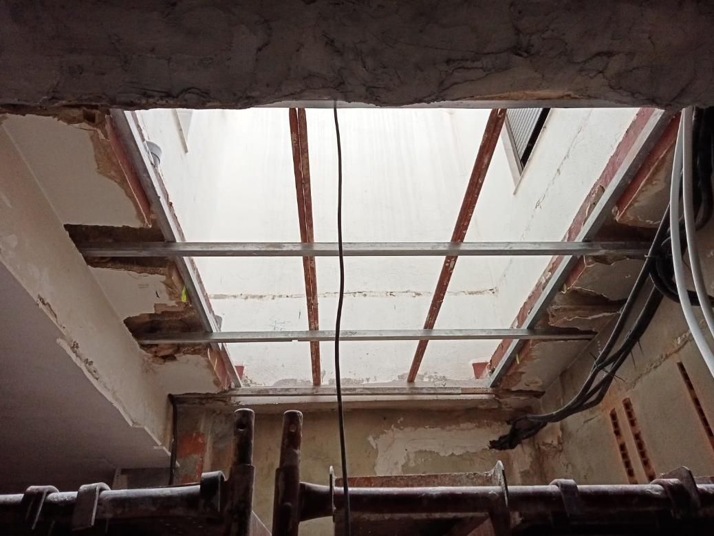 Abertura en el techo que deja al descubierto vigas metálicas y cableado. Paredes de ladrillo y blancas con escombros.