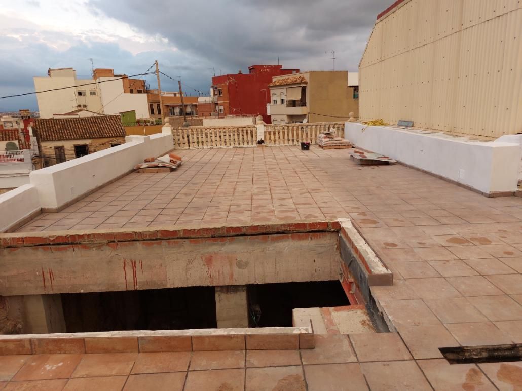 Azotea con tejas de terracota, paredes parciales de ladrillo y edificios de la ciudad al fondo bajo un cielo nublado.