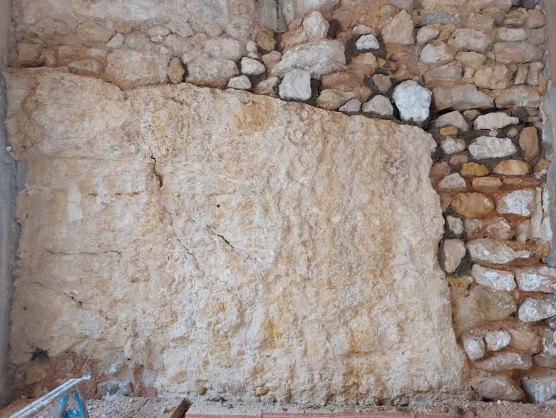 Muro de piedra con una gran mancha de color claro rodeada de piedras más pequeñas y mortero.