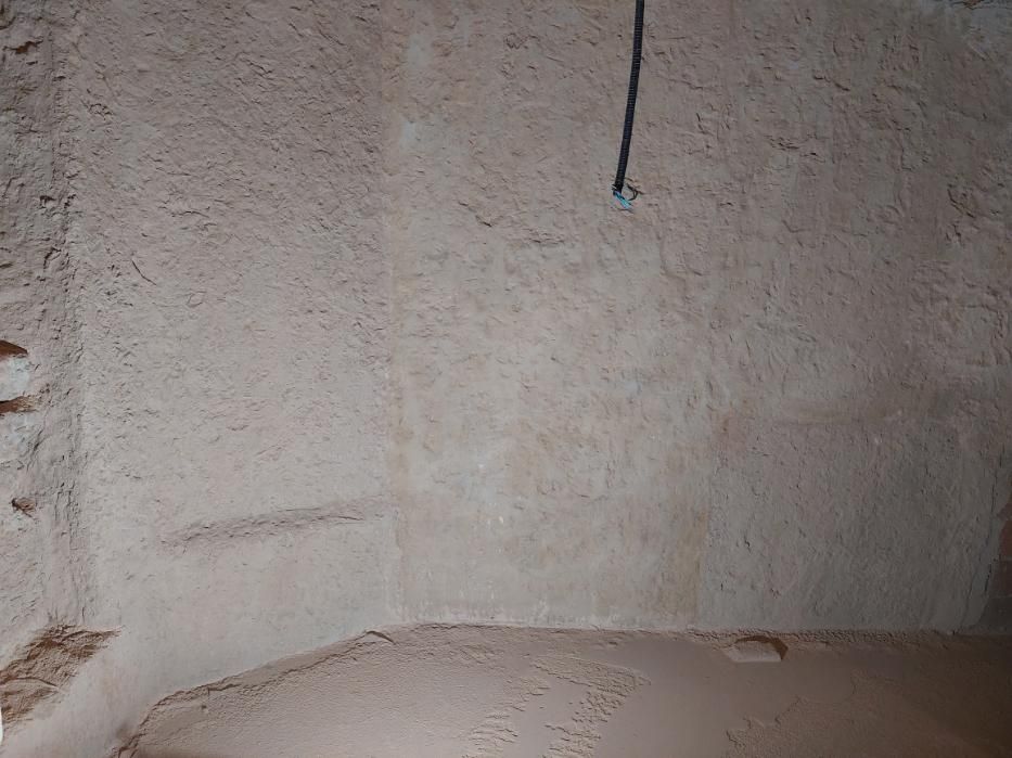 Vista interior de una pared y suelo de color marrón claro con textura rugosa. Un cable negro cuelga desde arriba.