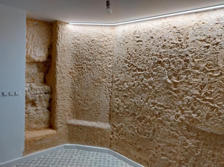 Esquina de una habitación con paredes de piedra tosca y color canela, estante empotrado