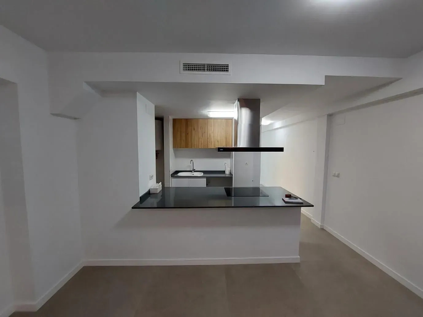 Cocina moderna con isla, campana de acero inoxidable, muebles de madera y paredes blancas.