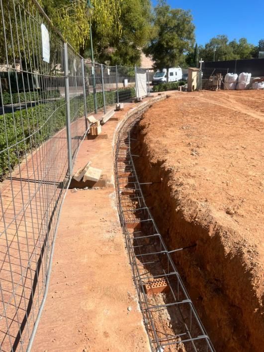 Sitio de construcción con zanja, estructura de varillas de refuerzo y cerca de alambre.