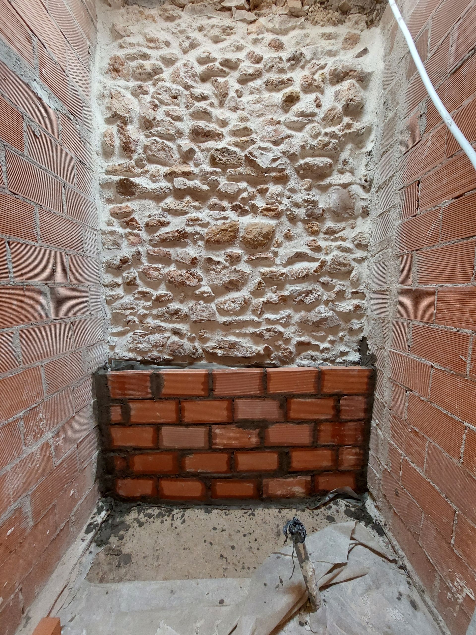 Construcción de muro de ladrillo y piedra en progreso dentro de un pequeño espacio cerrado.