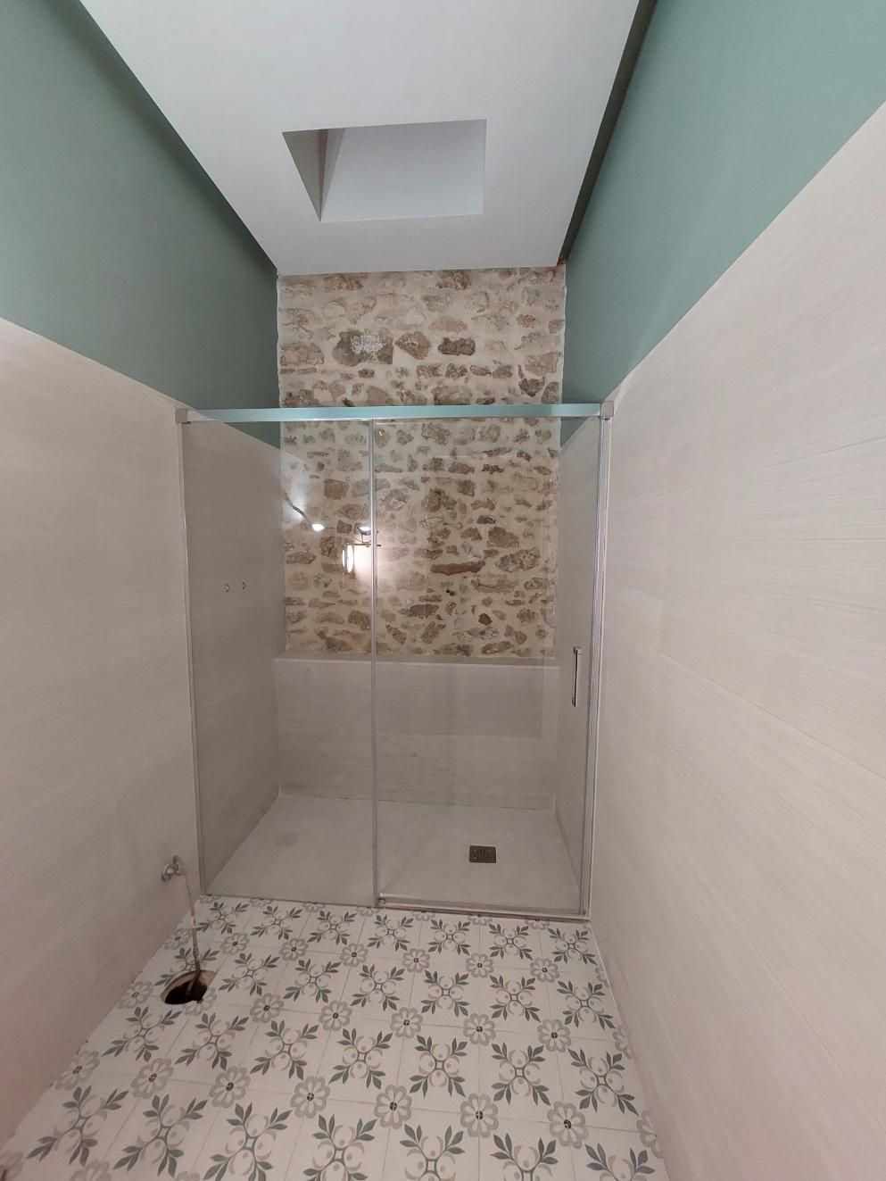 Ducha con puertas de vidrio transparente, fondo de pared de piedra, piso estampado