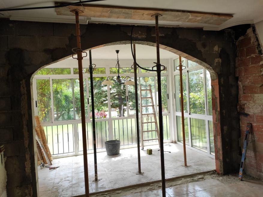 Construcción interior con arco, soportes temporales y eliminación parcial de paredes, que conduce a una terraza acristalada.