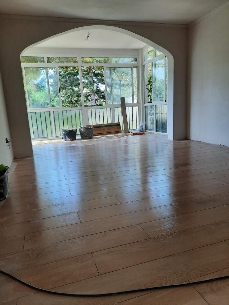 Habitación con pisos de madera nuevos, gran puerta arqueada a la terraza acristalada con barandillas blancas