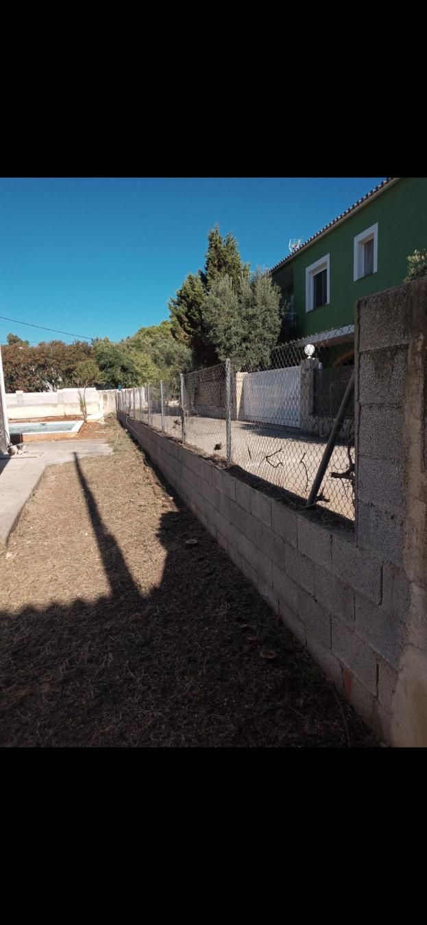 Un día soleado en un patio con un muro de hormigón, una valla y un edificio verde.