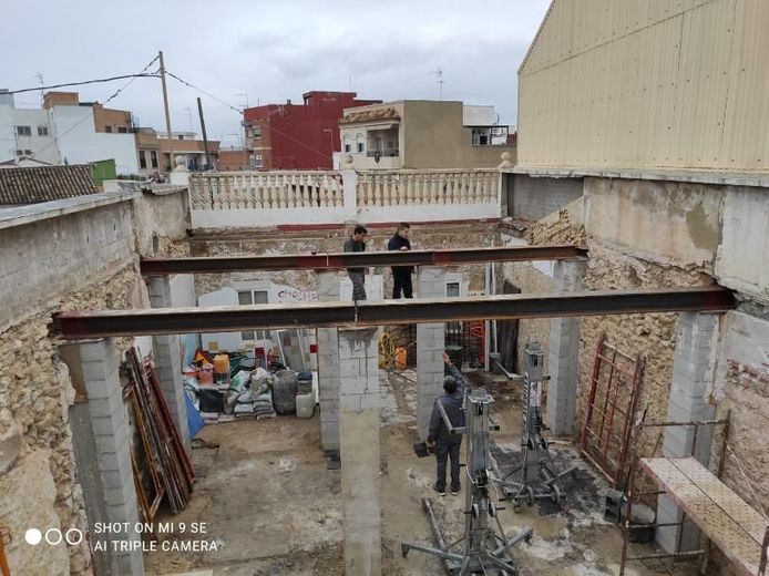 Sitio de construcción con trabajadores, vigas de soporte instaladas, estructura abierta.