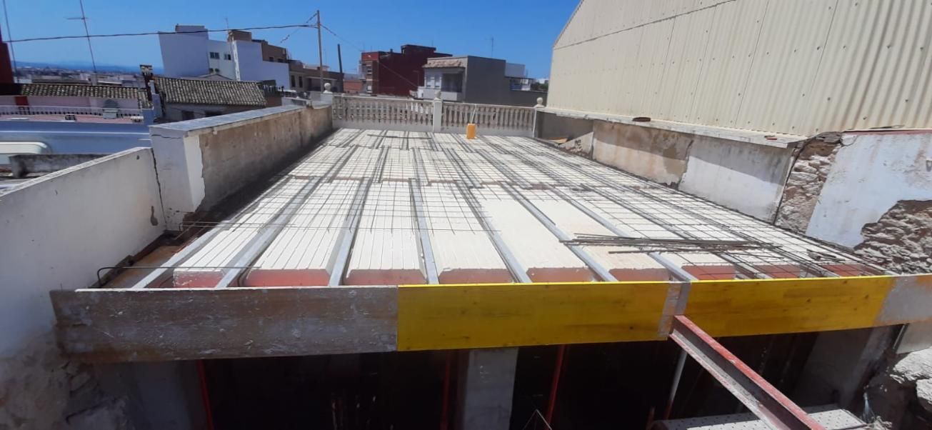 Obra en construcción con techo de hormigón parcialmente construido, se ven soportes de madera de color amarillo.