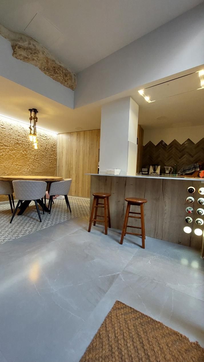 Cocina y comedor modernos con elementos de madera, piedra y azulejos. Dos taburetes de madera en la barra.