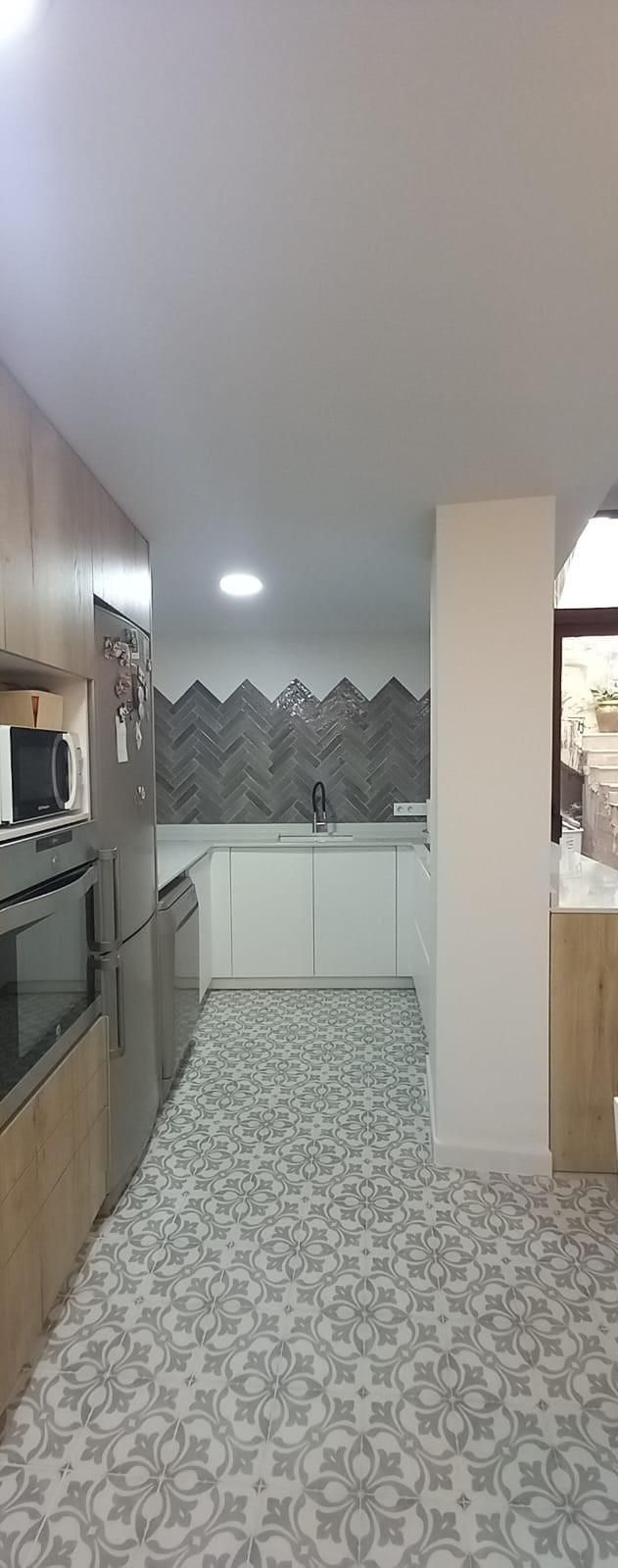 Cocina con gabinetes blancos, piso estampado y protector contra salpicaduras gris.