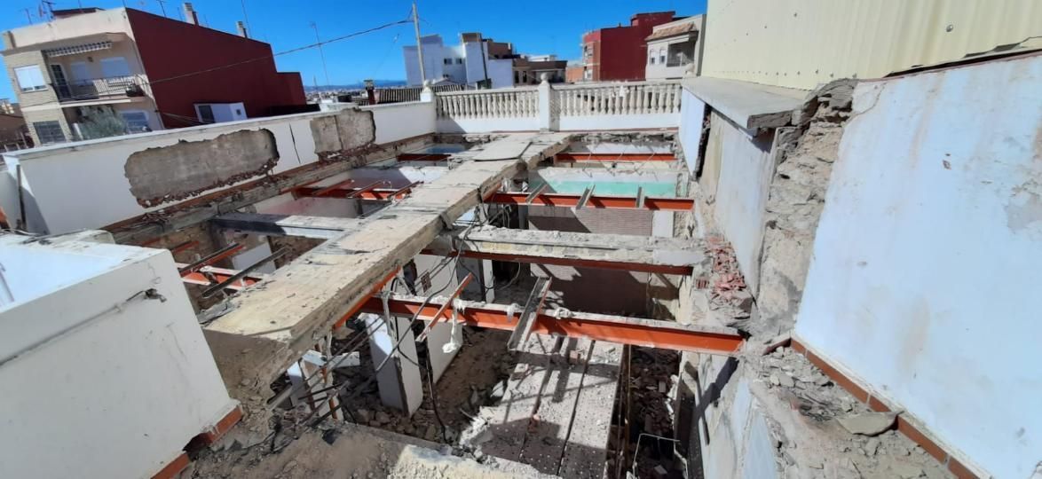 Sitio de construcción con vigas expuestas y escombros en un tejado, día soleado.