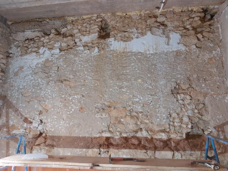 Muro en rehabilitación con piedra vista y yeso, parcialmente derribado.